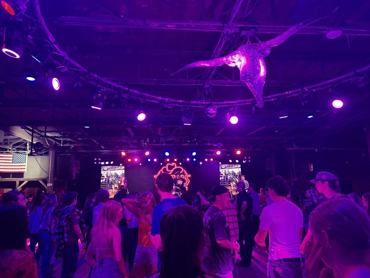 Under a long-horned bull shaped disco ball, a crowd dances to country music.